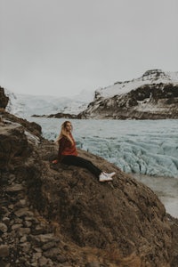 a woman sitting on a rock in front of a glacier