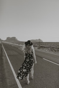 black and white photo of a woman walking down the road in a floral dress