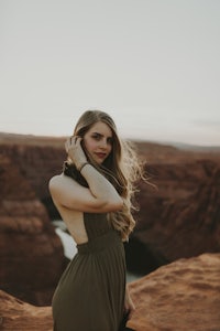 a woman in a green dress standing on a cliff at sunset