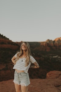 a woman in denim shorts standing on a rock in sedona, arizona