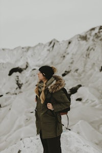 a woman in a green jacket standing on top of a snowy mountain