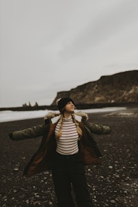 a woman with her arms outstretched on a black sand beach