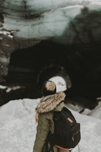 a woman with a backpack standing in front of an ice cave