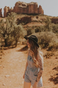 a woman wearing a hat and a romper walking down a dirt road in sedona, arizona