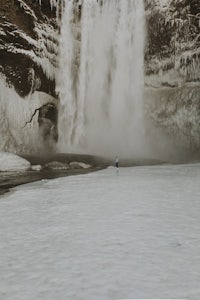 a person is standing in front of a waterfall in iceland