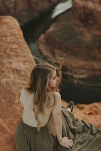 a woman sitting on top of a cliff overlooking a canyon